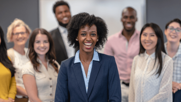 Black woman looking at camera with diverse group of people in background look at camera