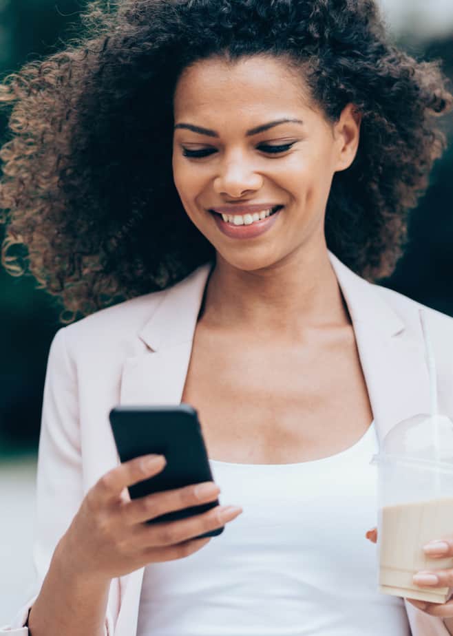 black woman looking at her phone while holding a coffee